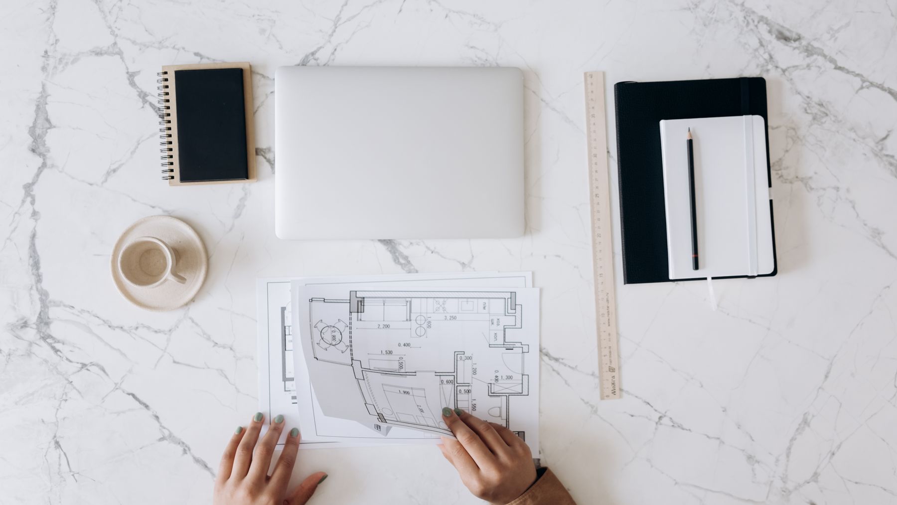 Architectural drawings, a laptop, measuring tools, and a notebook arranged on a work table